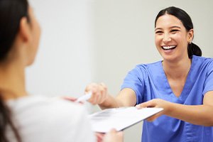 Dental staff in Matthews smiling at patient while handing over financing paperwork