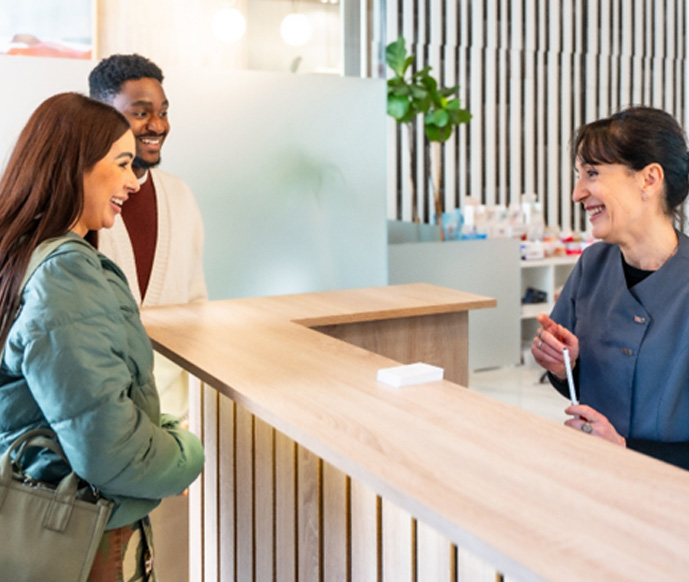 Dental receptionist smiling at couple in lobby