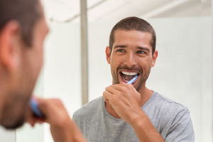 Man smiling while brushing his teeth in bathroom