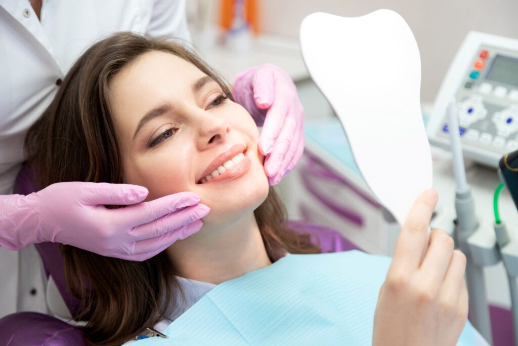 Woman in dental chair smiling at mirror with dentist in purple gloves touching her cheeks