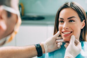 Woman smiling in dentist's chair while dentist examines smile. 